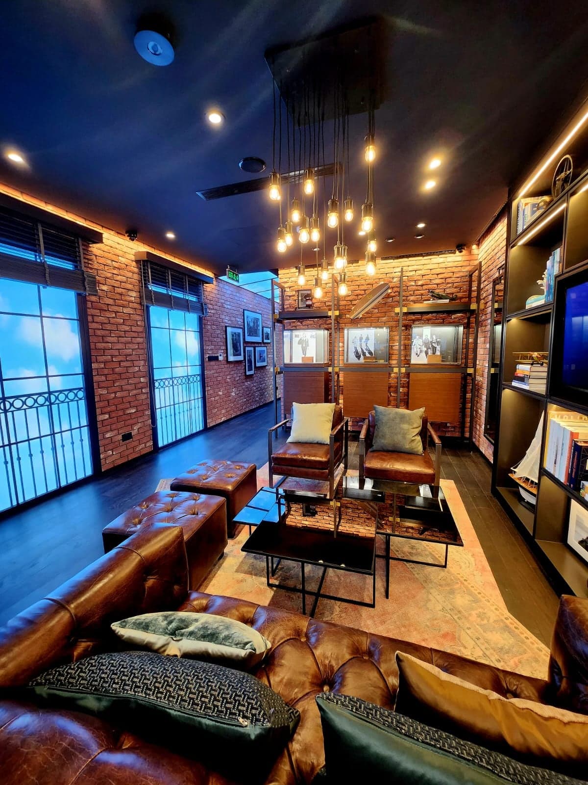 Boutique lounge with brick walls, leather seating and a cluster of filament pendants, with lit display shelving along one side