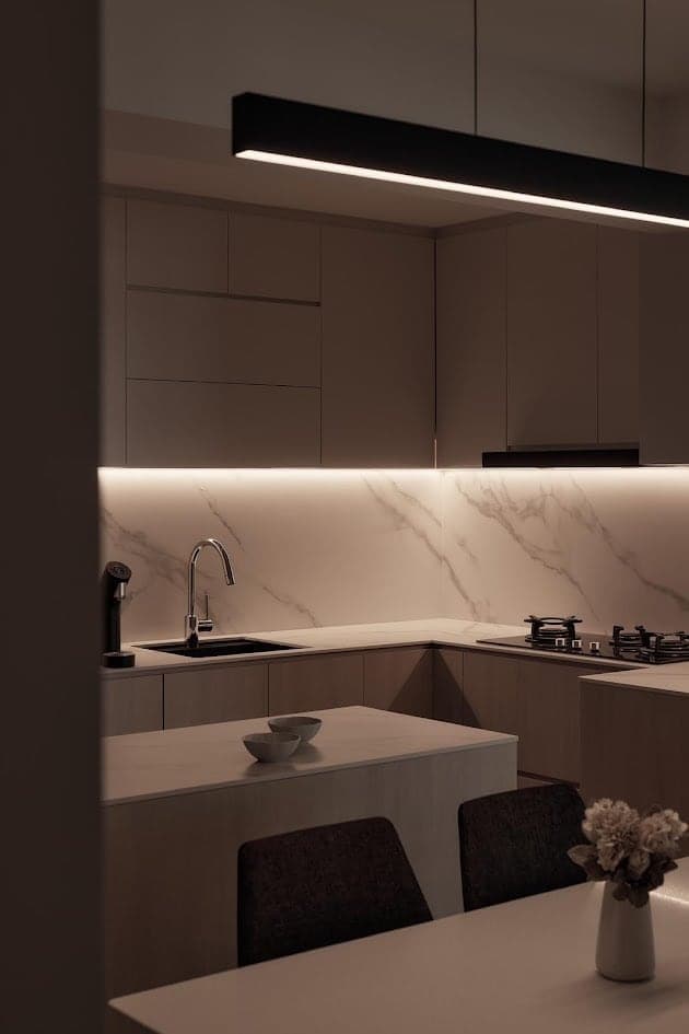 Kitchen with a linear pendant over the island and under-cabinet light across a marble splashback